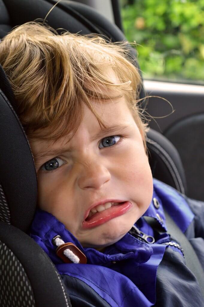 A family road trip packing list- photo of an unhappy boy in a car seat.